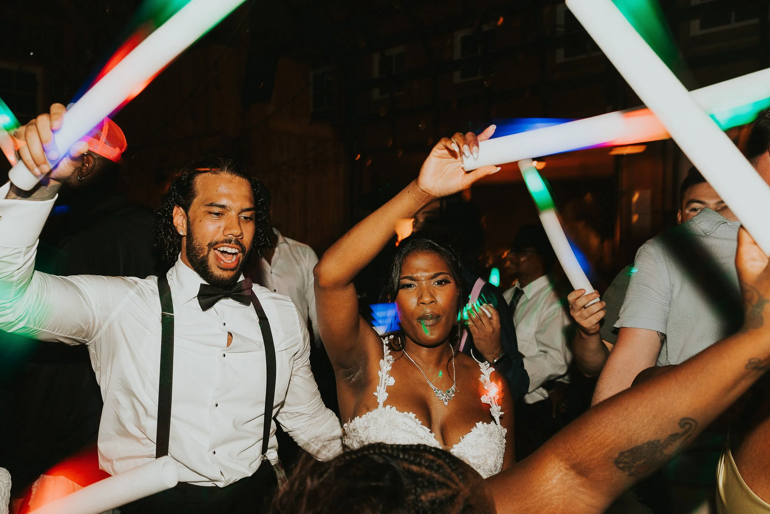A group of people dancing at a party while holding glow sticks.