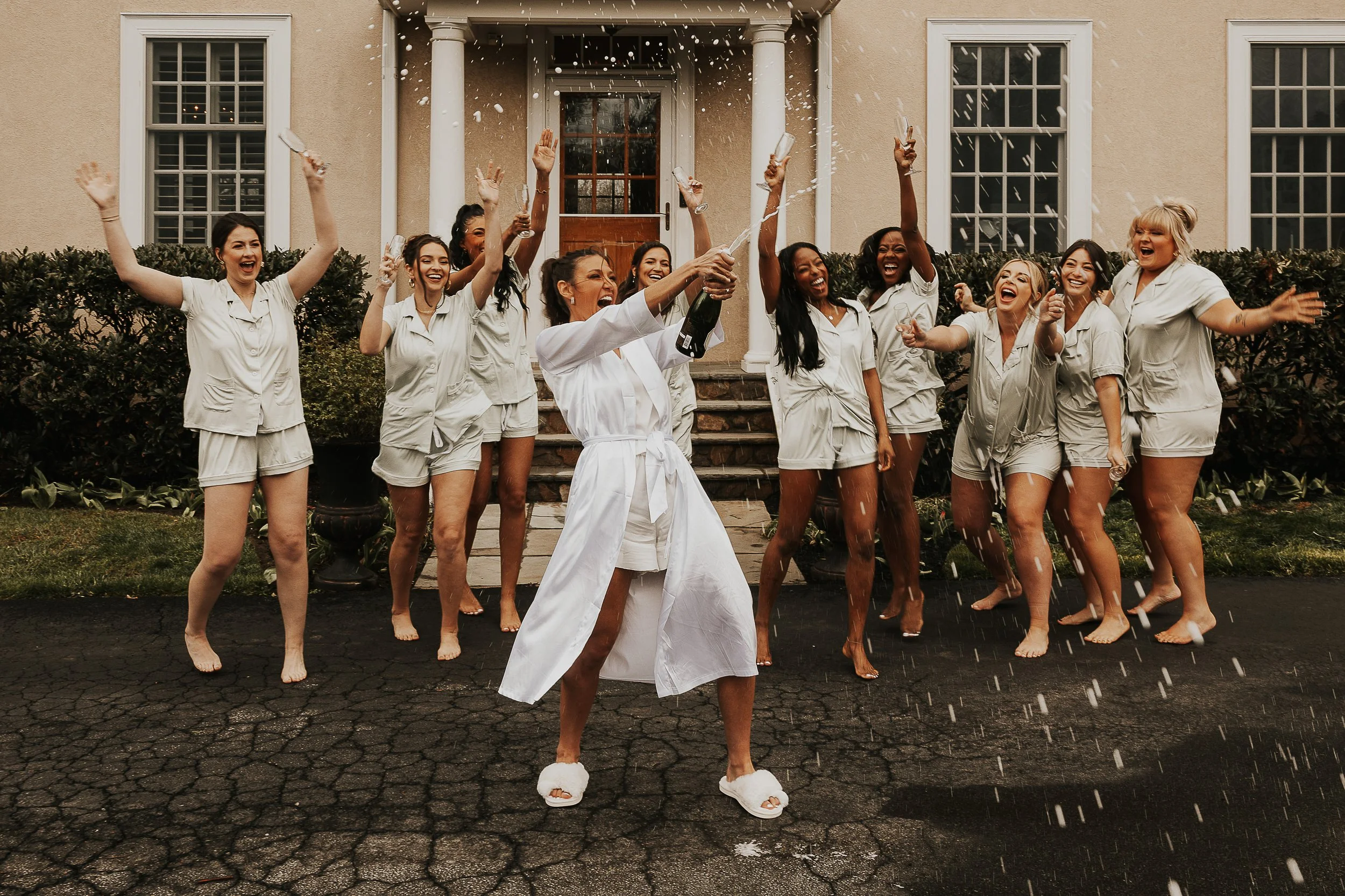 A group of women in pajamas celebrating outside a house with champagne and confetti.