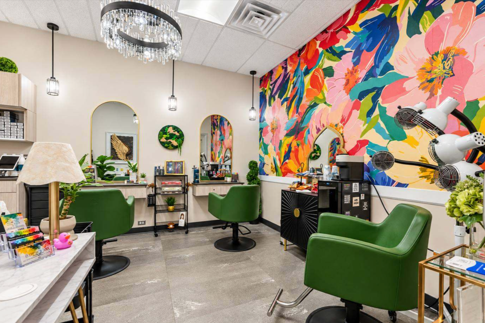 A colorful interior of a salon with a vibrant floral mural on the wall, green chairs, mirrors, salon equipment, and decorative plants.