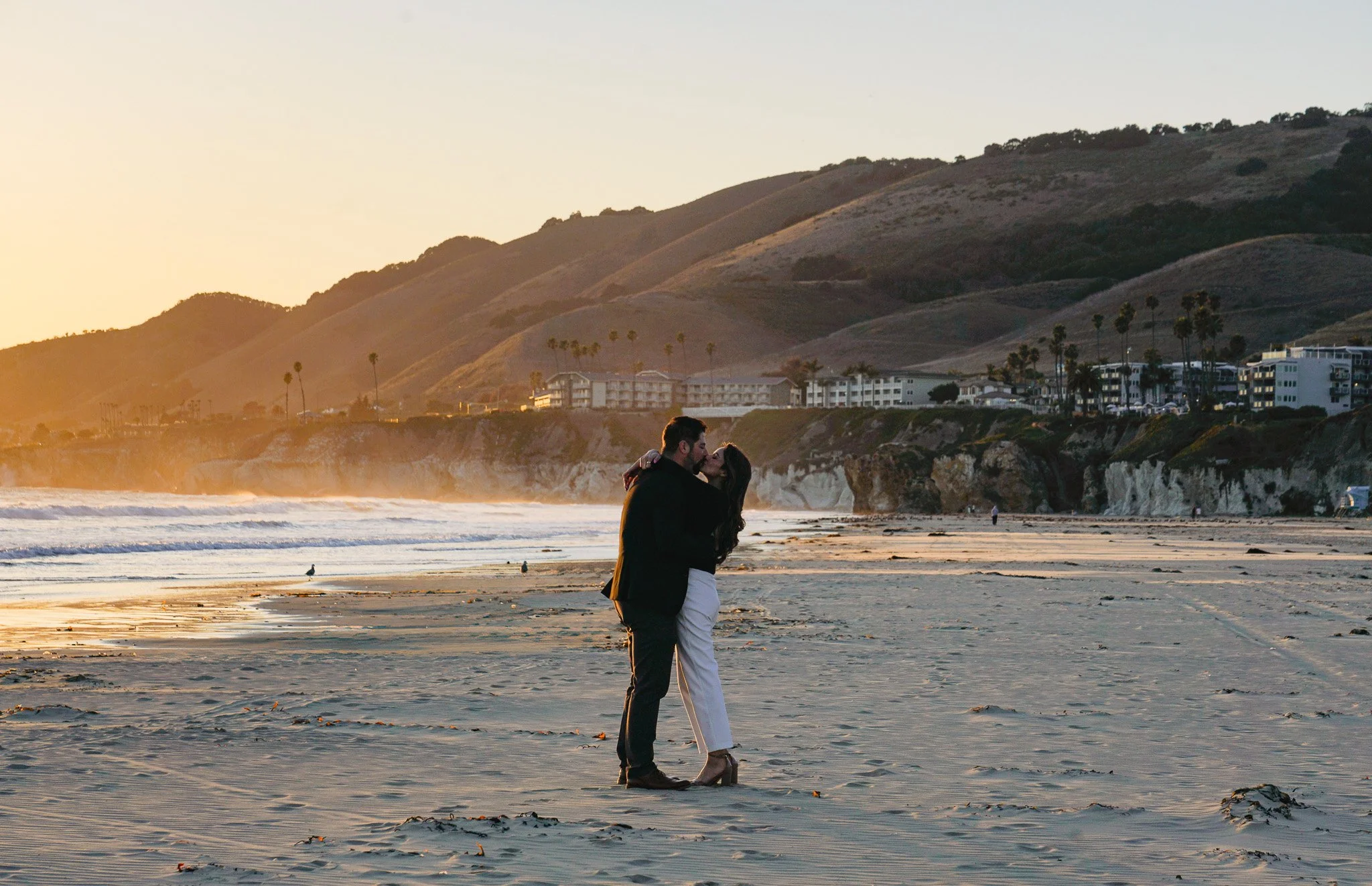 Couple sharing a sunset kiss on a Central Coast beach during a romantic proposal or elopement session.