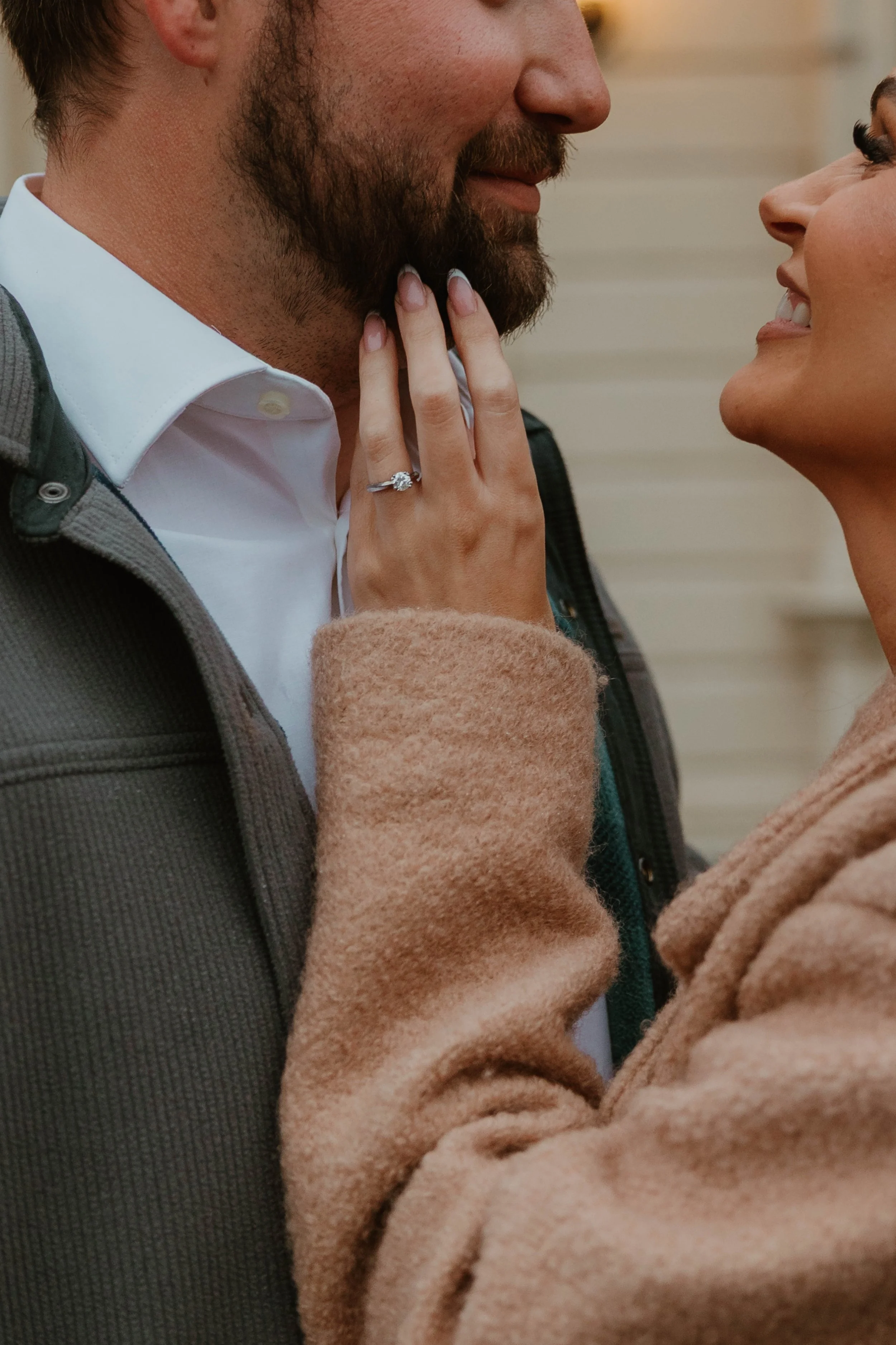 Close-up of a couple engaging in a romantic moment; the woman is touching the man's beard and wearing a ring, smiling at each other.