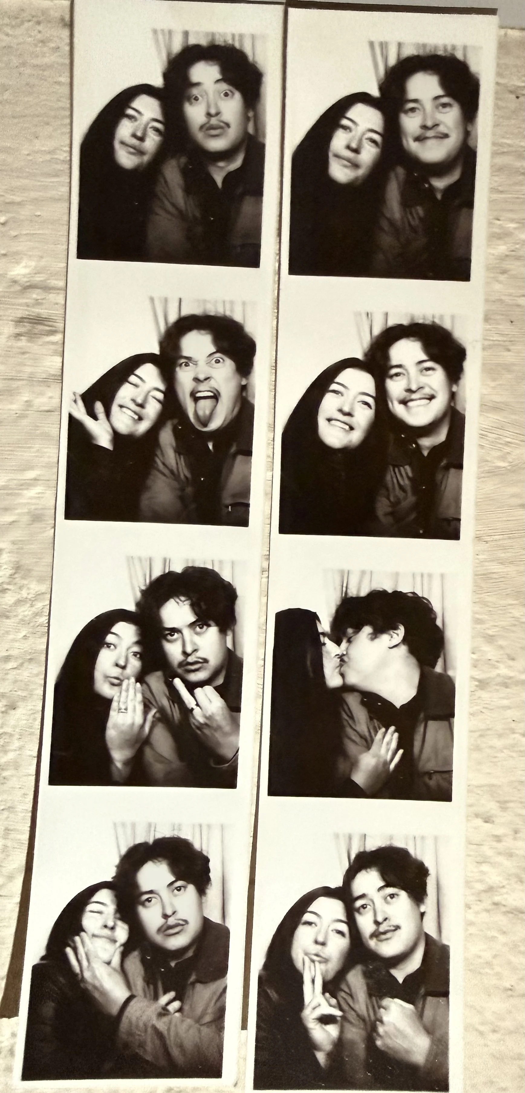 Strip of four black-and-white photo booth pictures of a man and woman making various facial expressions and poses, including kissing.