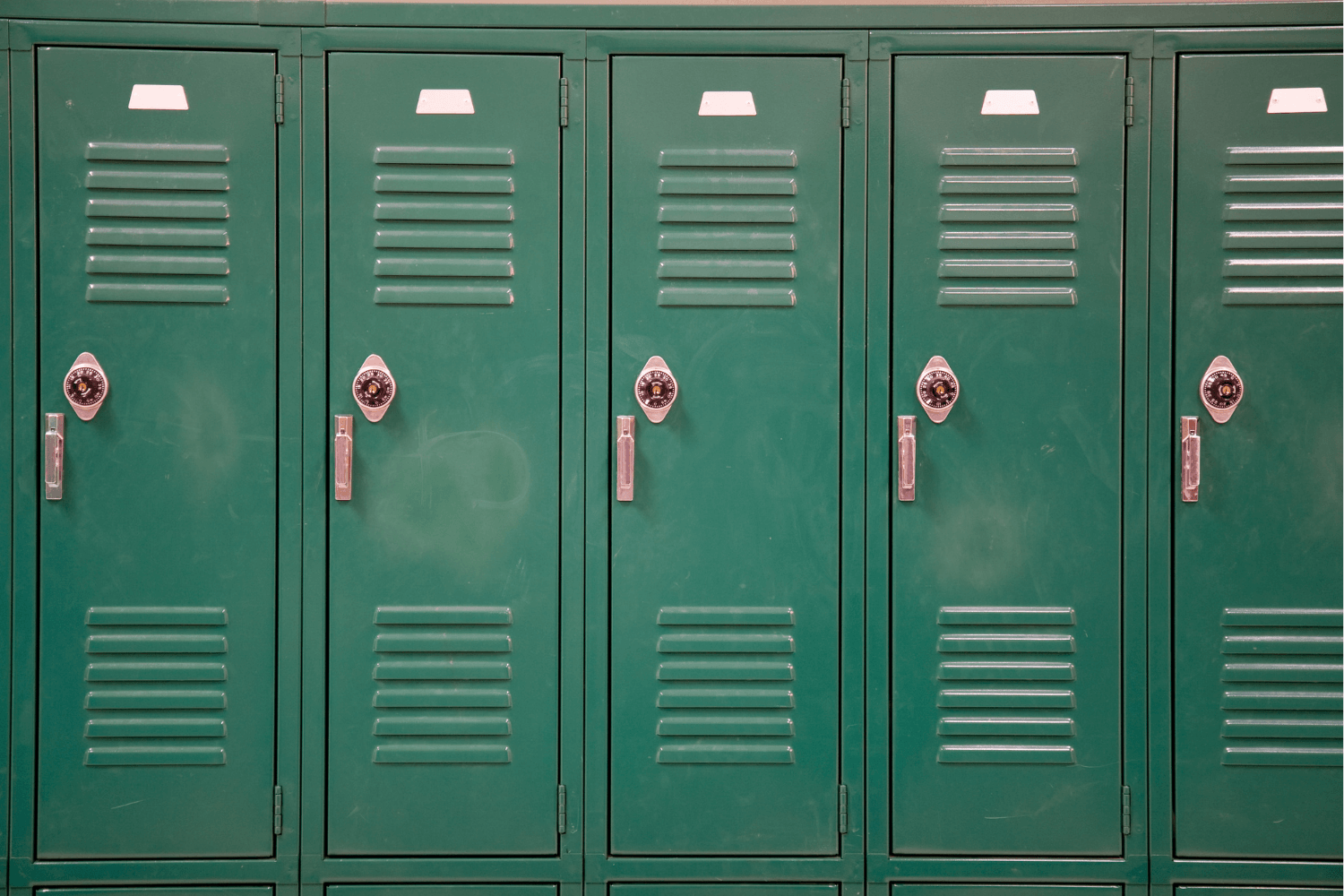 A row of green metal school lockers with ventilation slots, combination locks, and handles.