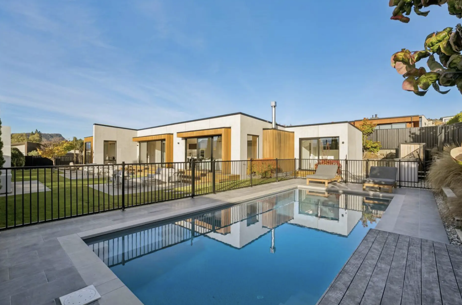 An exterior shot looking over an outdoor pool towards the landscaped Sapphire Spring Retreat a Wanaka holiday home managed by Be Our Guest