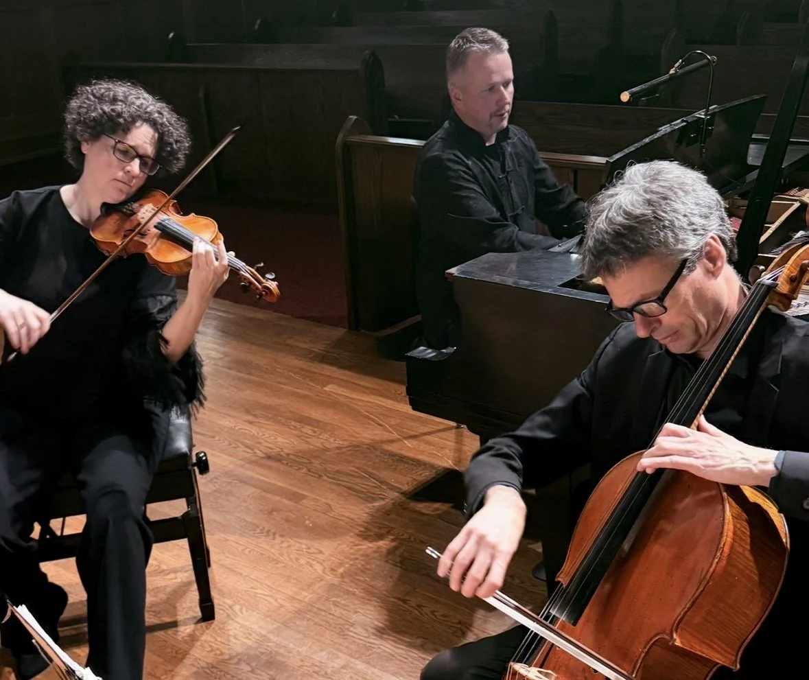 Two musicians playing string instruments and a pianist playing a grand piano in a dimly lit room.