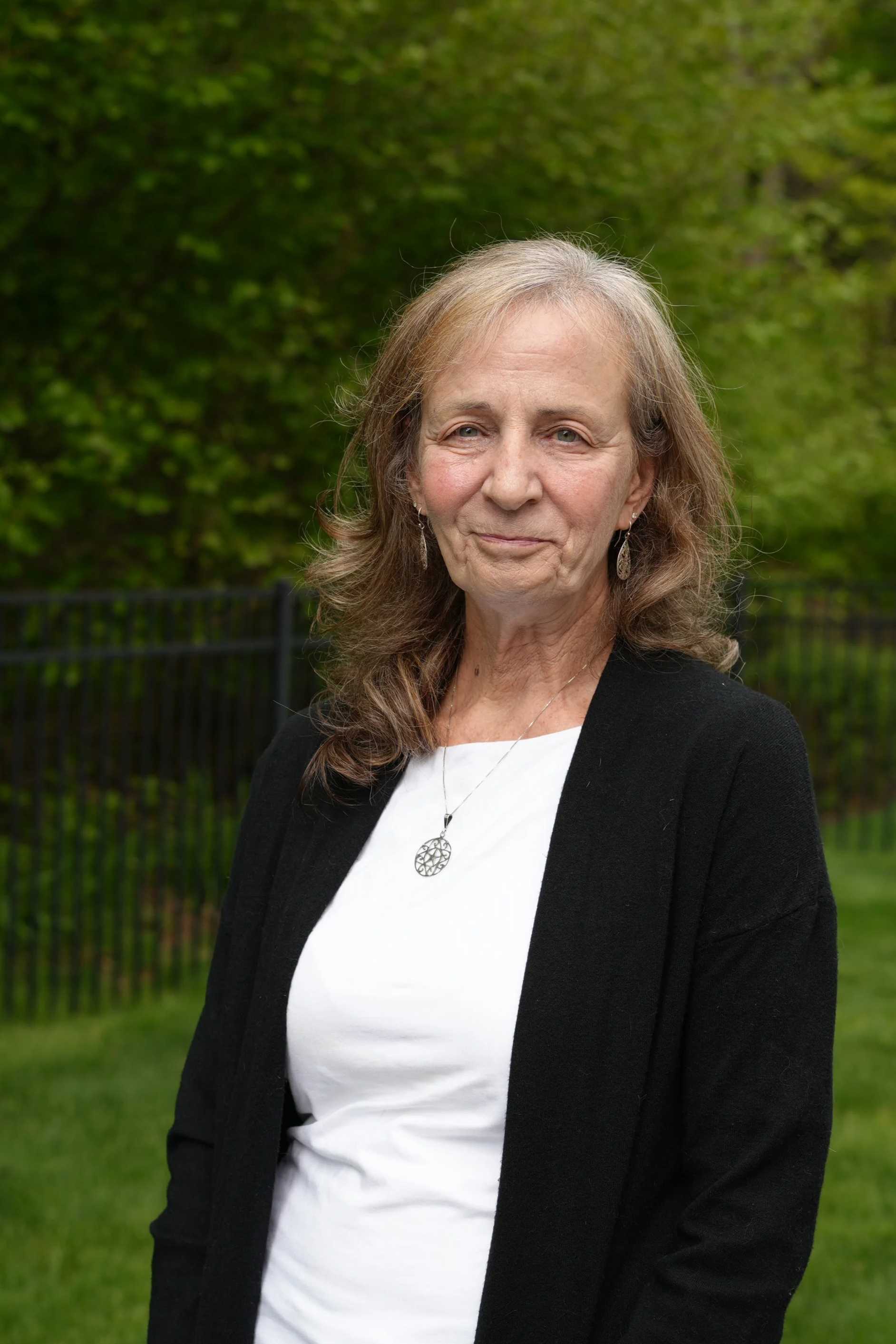 A woman wearing a white top, black blazer, and silver earrings, standing outdoors.
