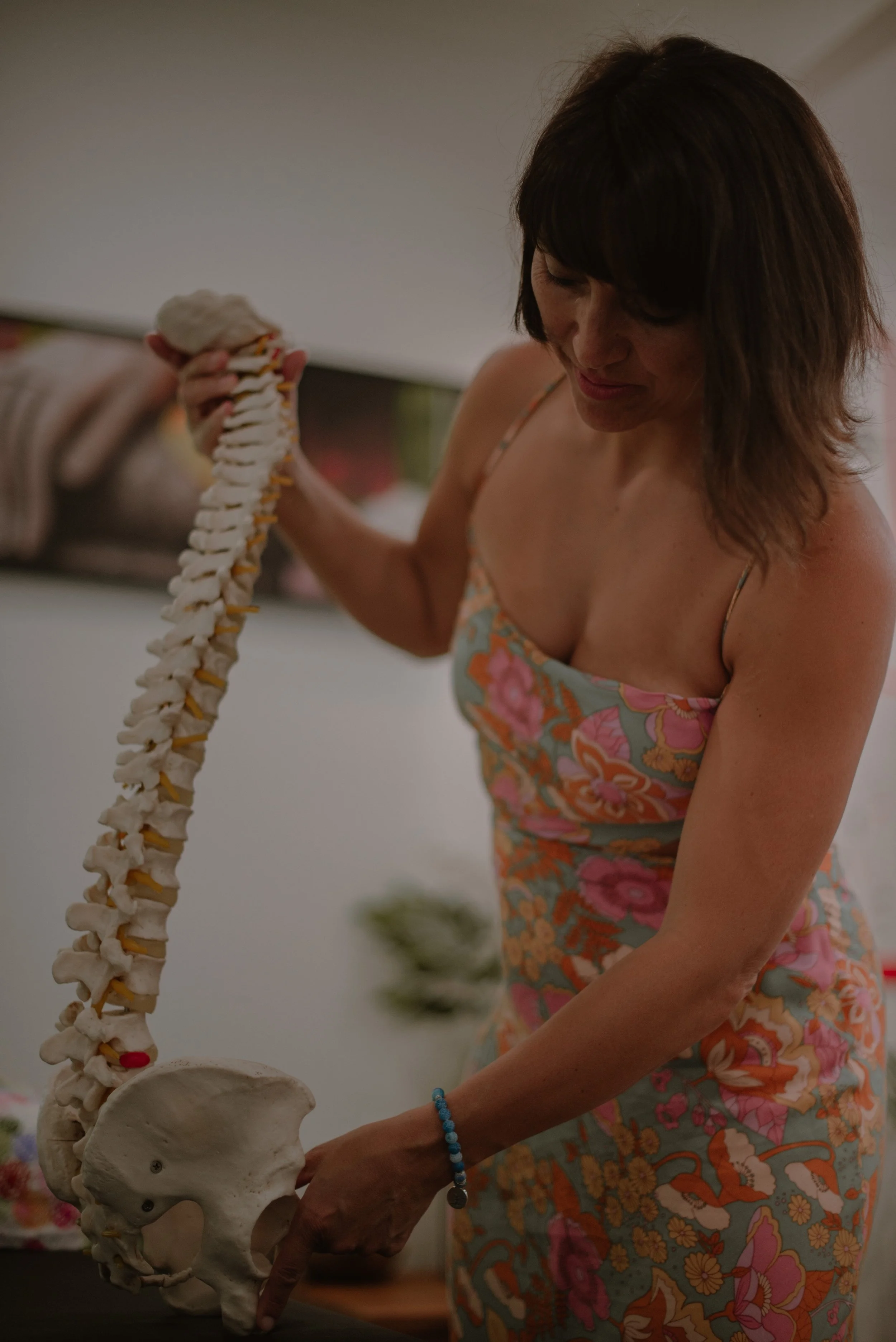 A woman holding a human spine model in a room with a blurred background.