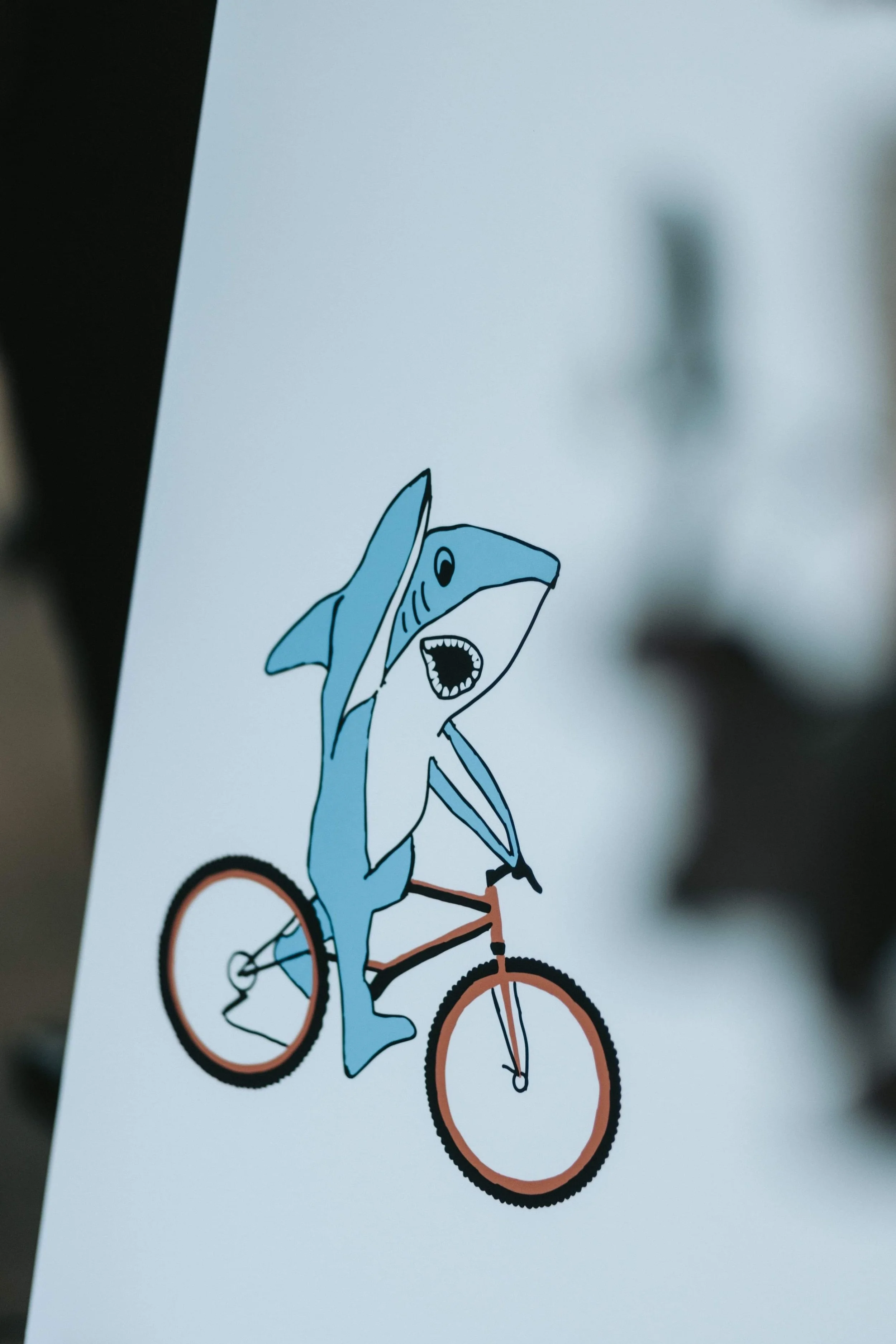 A cartoon shark riding a bicycle, shouting with its mouth open, on a white background.