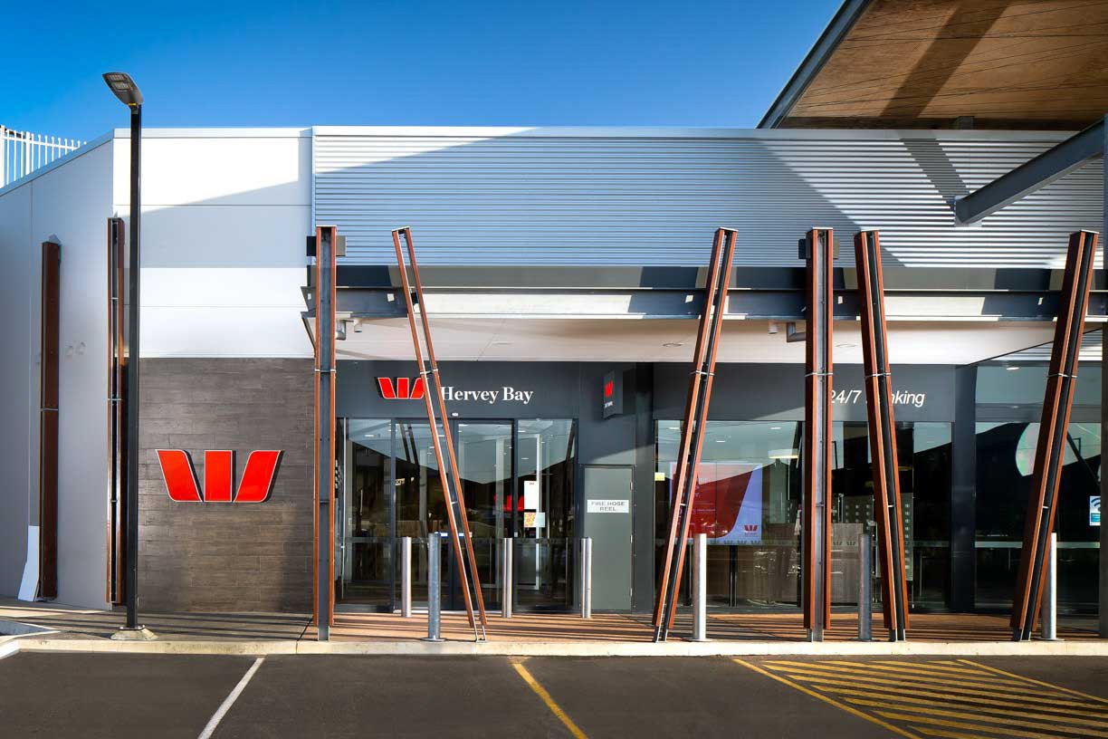 Exterior view of Westpac Bank branch at Hervey Bay with prominent red Westpac logo, glass entrance doors, and modern architectural design including vertical metal supports and a covered walkway.