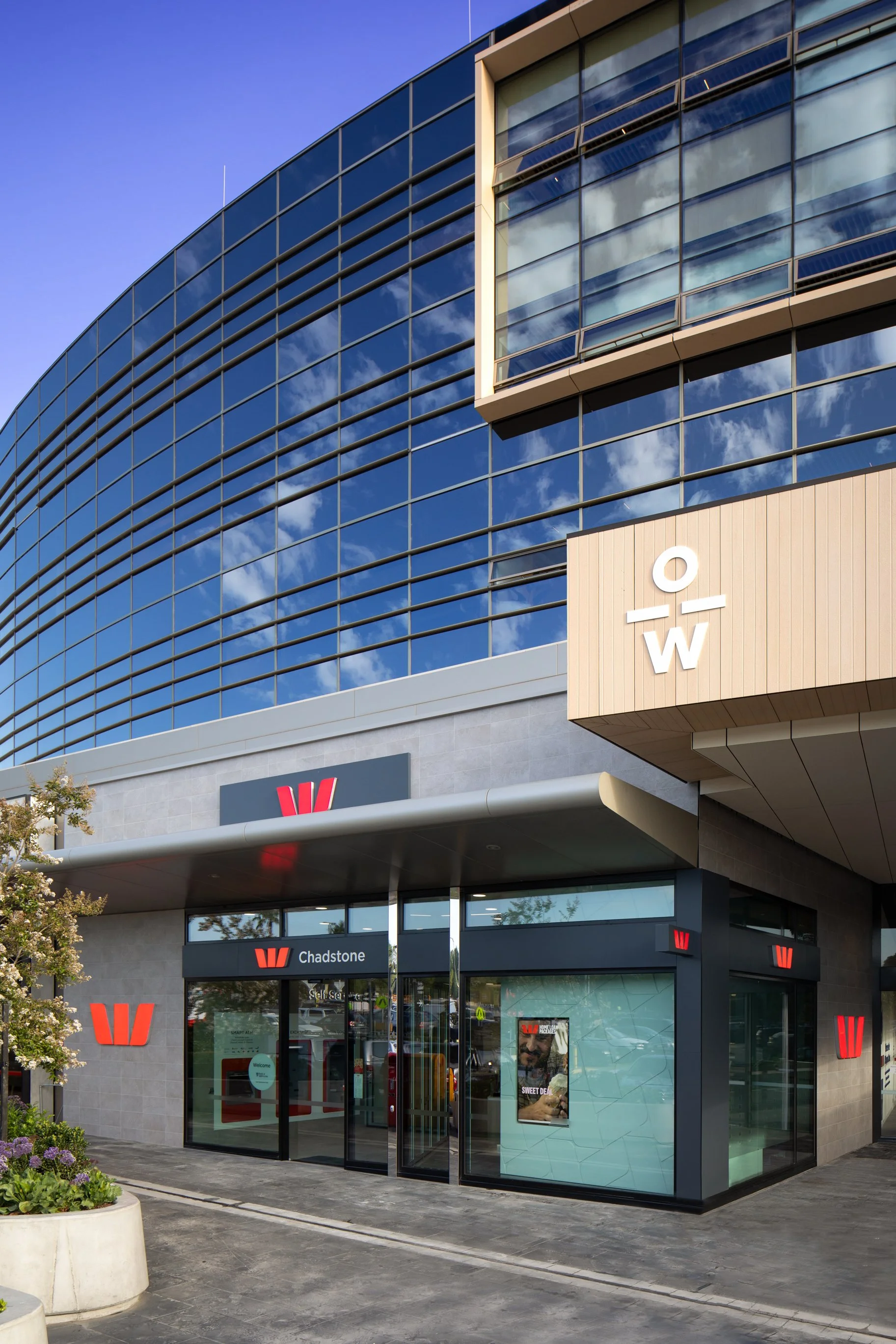 Exterior of a Westpac bank branch with glass windows, signage, and a branded storefront in a shopping center.