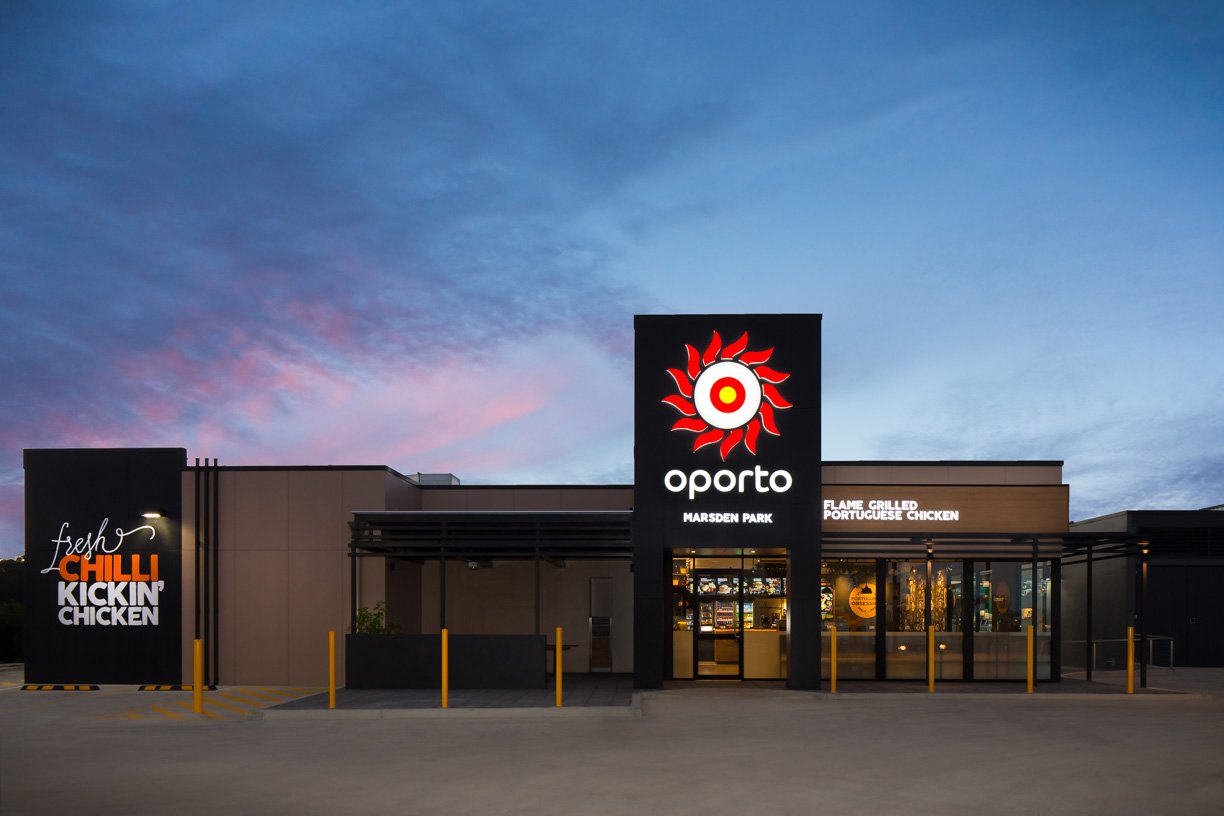 Front view of a restaurant called Aporto at Marsden Park during twilight, featuring signs with a sun and target logo and phrases like 'fresh chilli kickin' chicken' and 'flame grilled Portuguese chicken'.