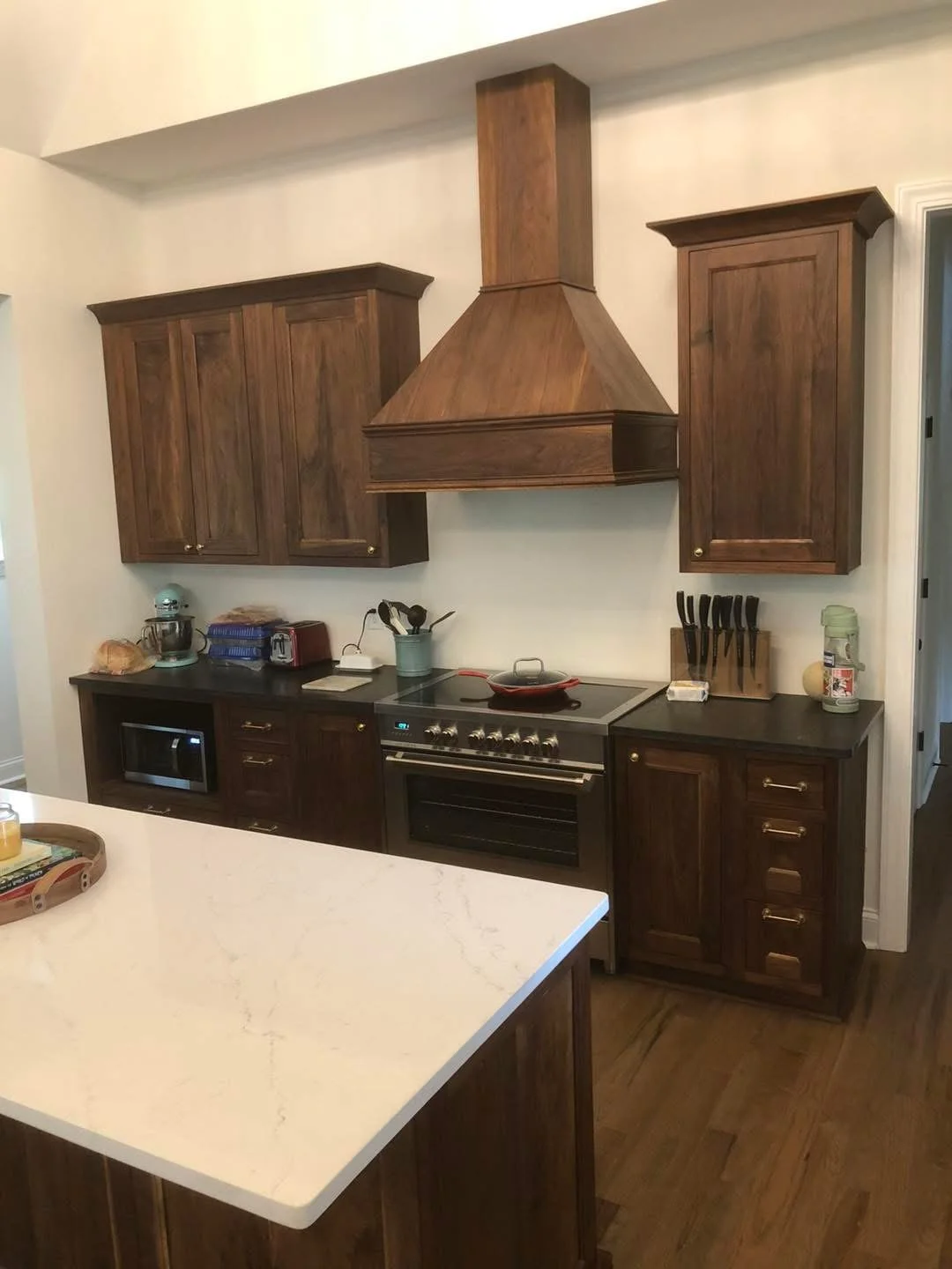 Kitchen with wooden cabinets, black countertop, stove, microwave, knife block, and countertop appliances.