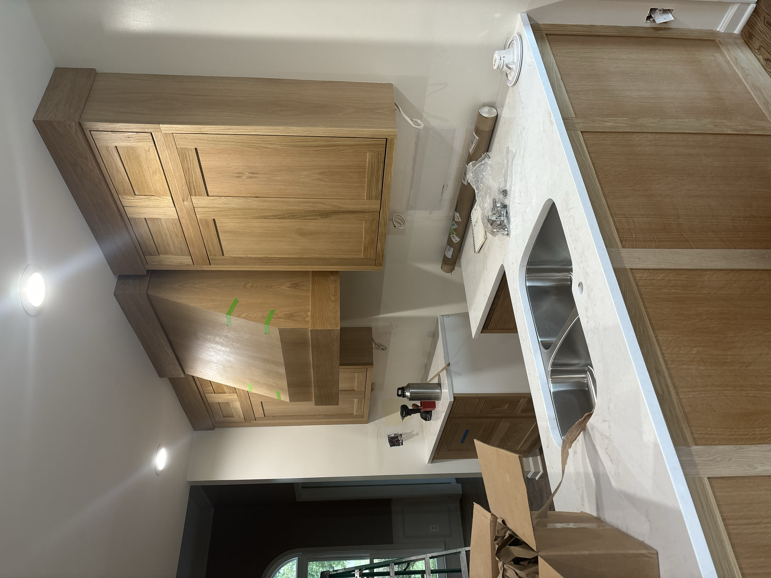 Unfinished kitchen with wooden cabinets, white countertops, a built-in sink, and various construction tools and materials.