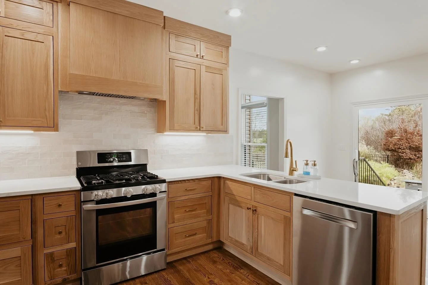 Kitchen with wooden cabinets, stainless steel stove, white countertop, and double sink near window and sliding door to outside.