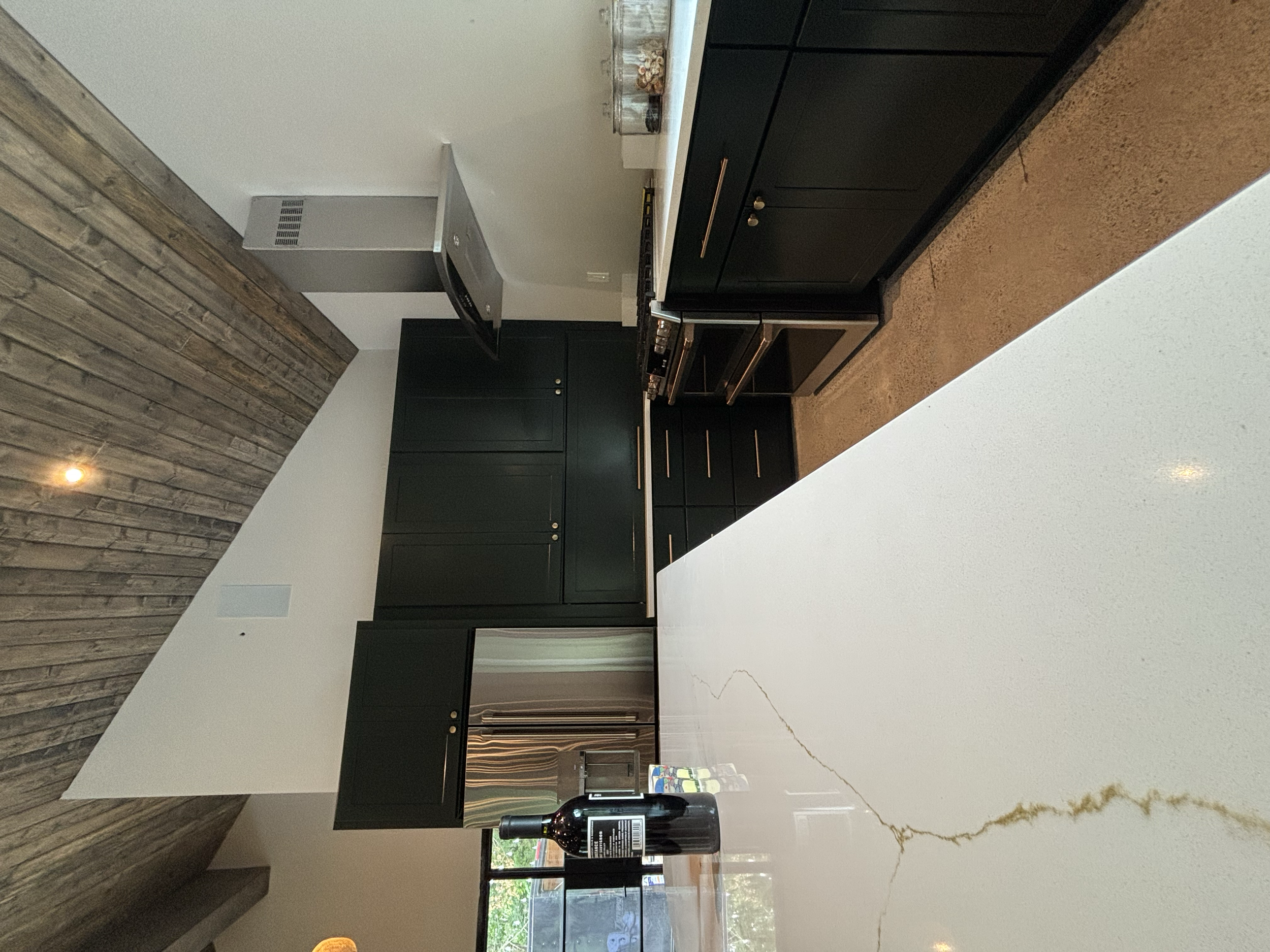 Modern kitchen with black cabinets, a white marble island, and a wooden accent wall with a single ceiling light.