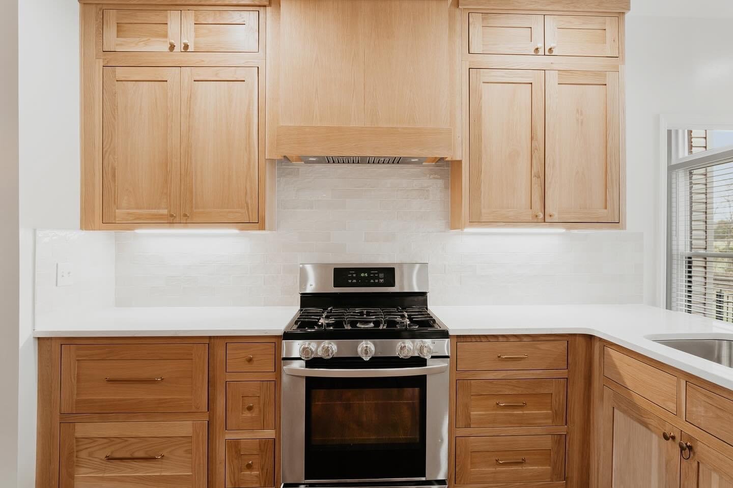 Kitchen with light wooden cabinets, white countertops, a stainless steel stove, and a window with blinds.