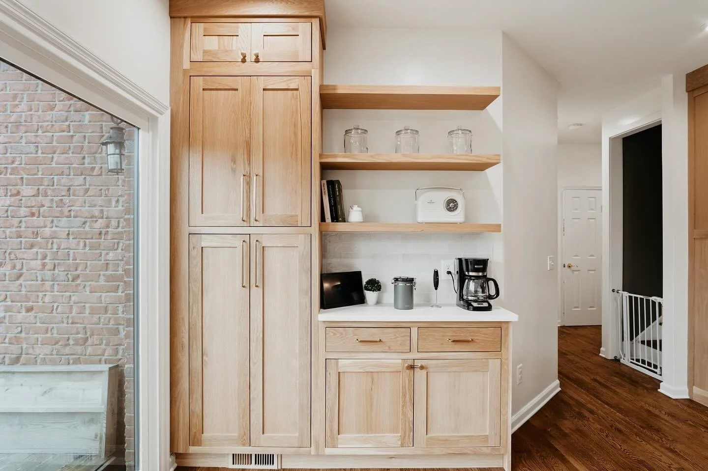 Wood cabinetry and open shelves in a kitchen area, with a coffee maker, small plant, and other kitchen items on the counter.