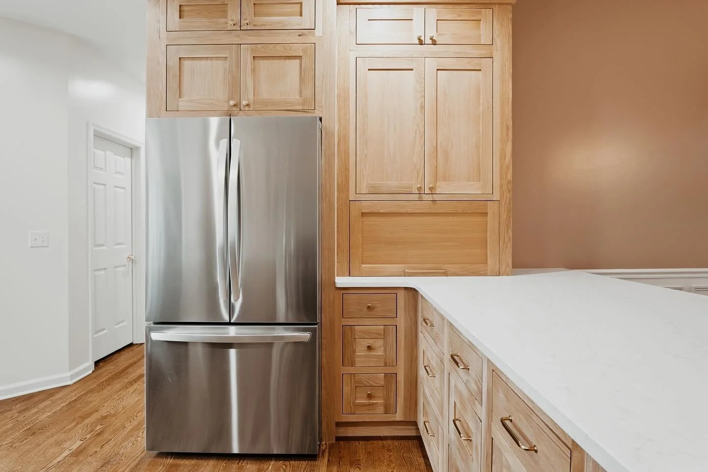 Stainless steel refrigerator next to wooden kitchen cabinets with a white countertop and a brown wall.