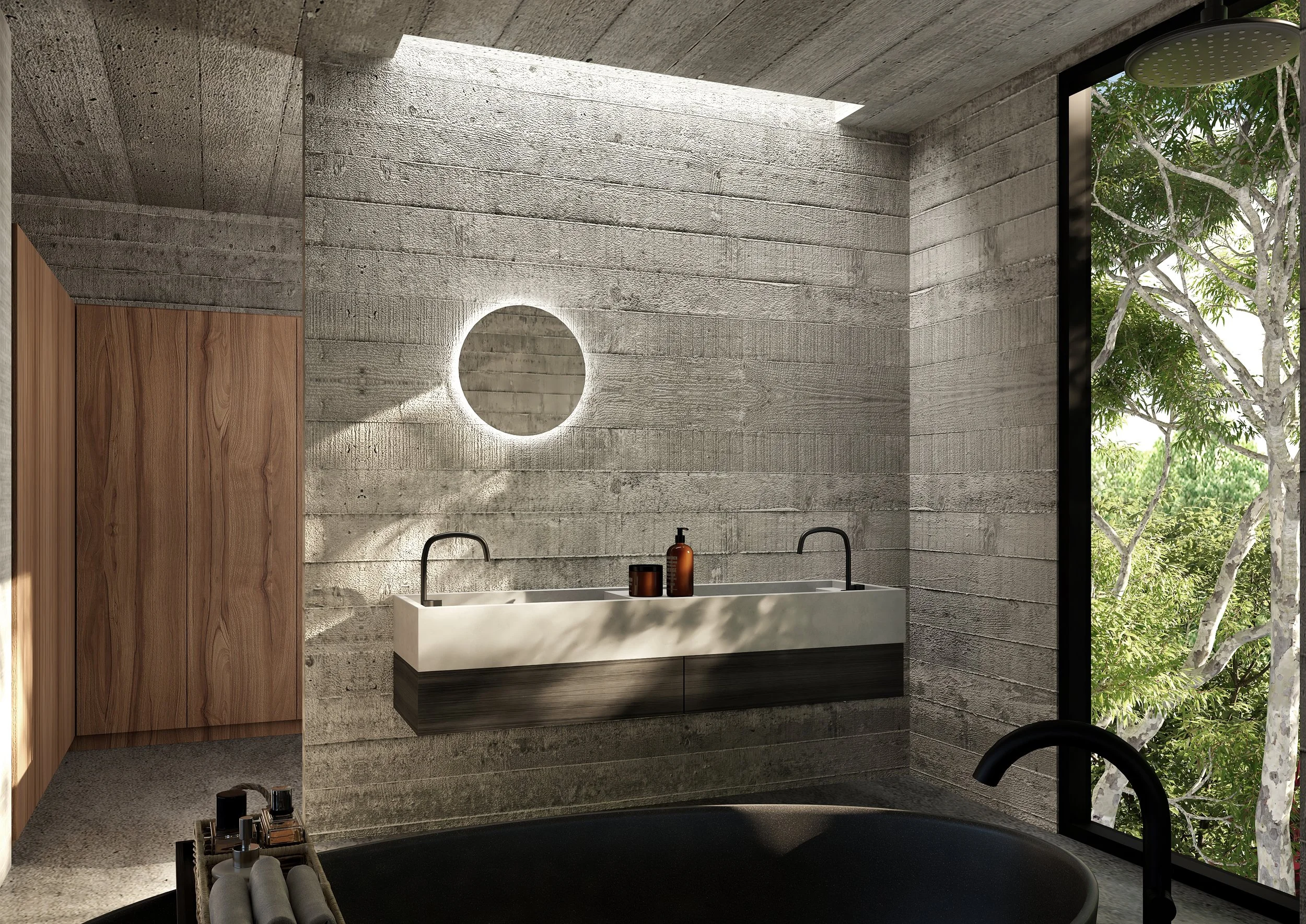Modern bathroom with concrete walls, large window revealing trees outside, a round illuminated mirror, a white vessel sink with black cabinets underneath, and a black freestanding bathtub in the foreground.