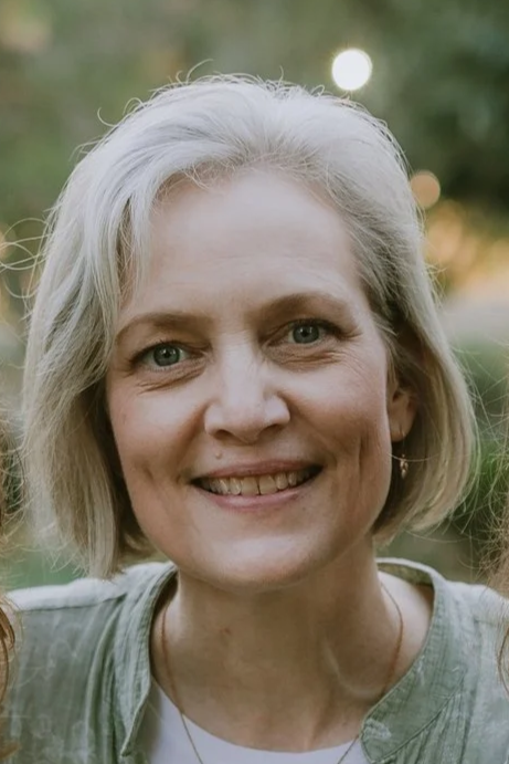 A smiling middle-aged woman with short gray hair outdoors during sunset.