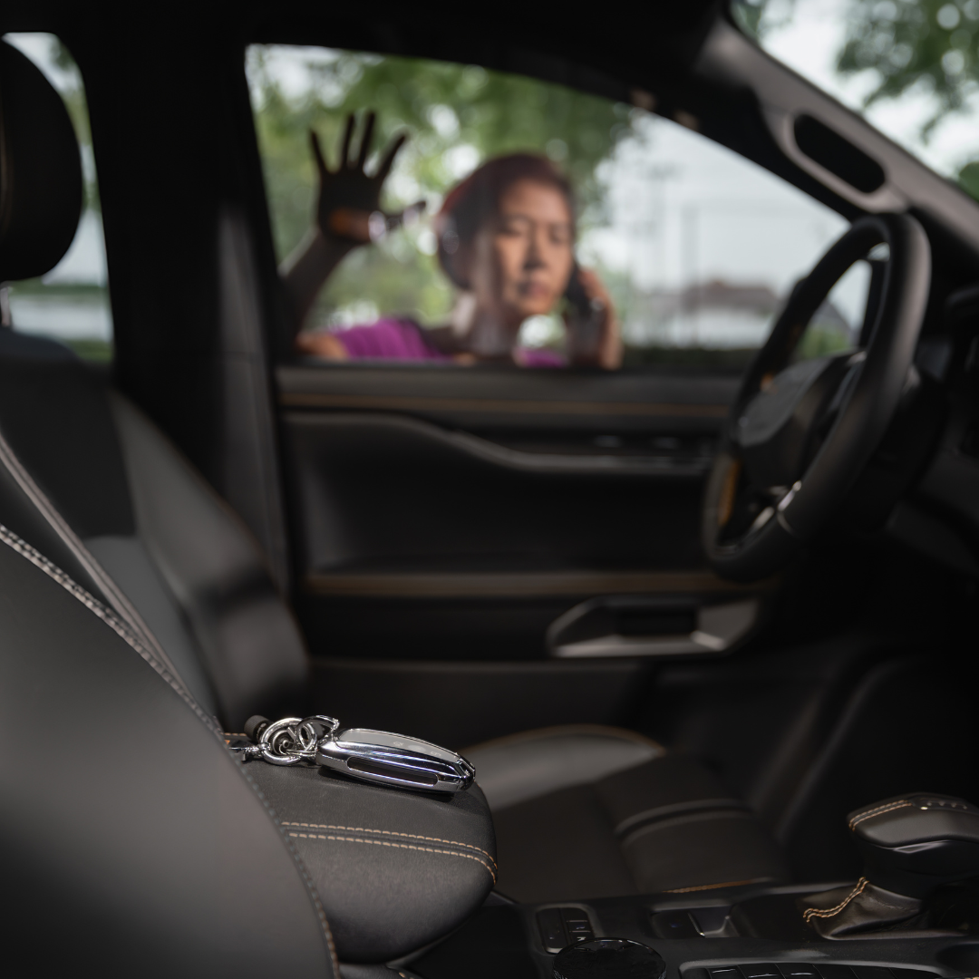 Car interior with a set of car keys on the front passenger seat and a woman with brown hair, wearing a purple top, talking on a cellphone outside the driver-side window.