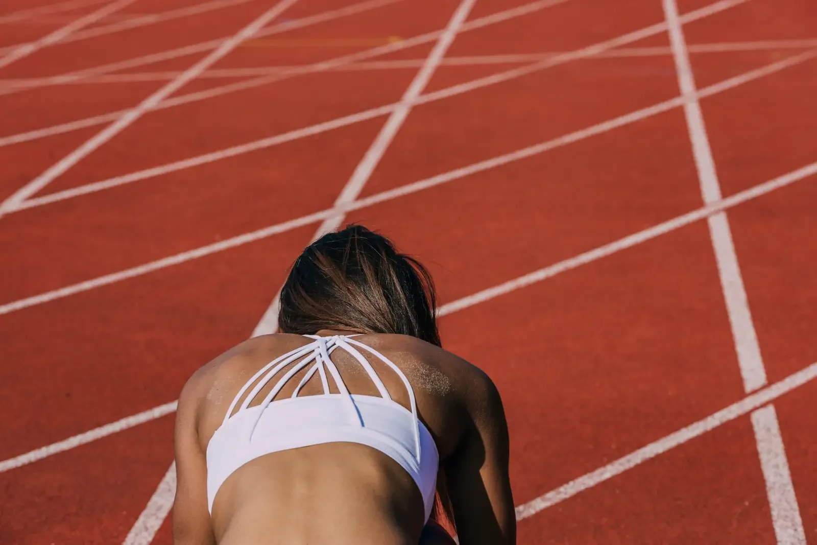 Former athlete crouched on a running track, appearing exhausted and overwhelmed after pushing through physical and emotional burnout.