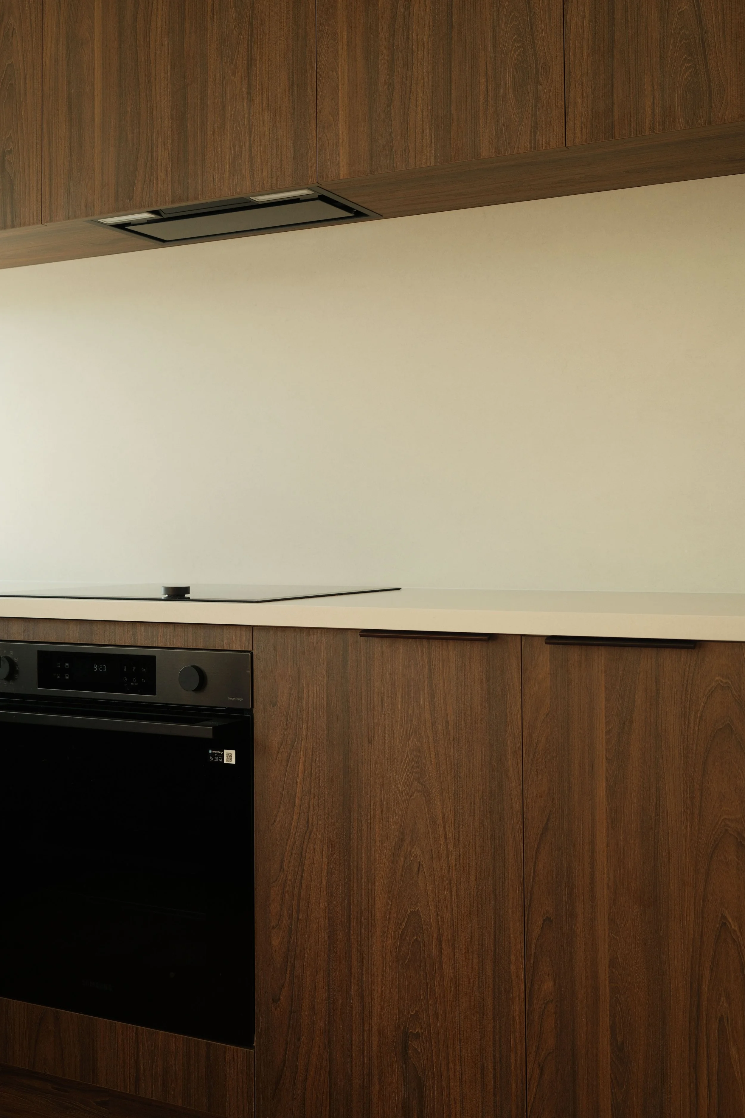 Mount Maunganui modern kitchen with wooden cabinets and black oven below a white countertop.