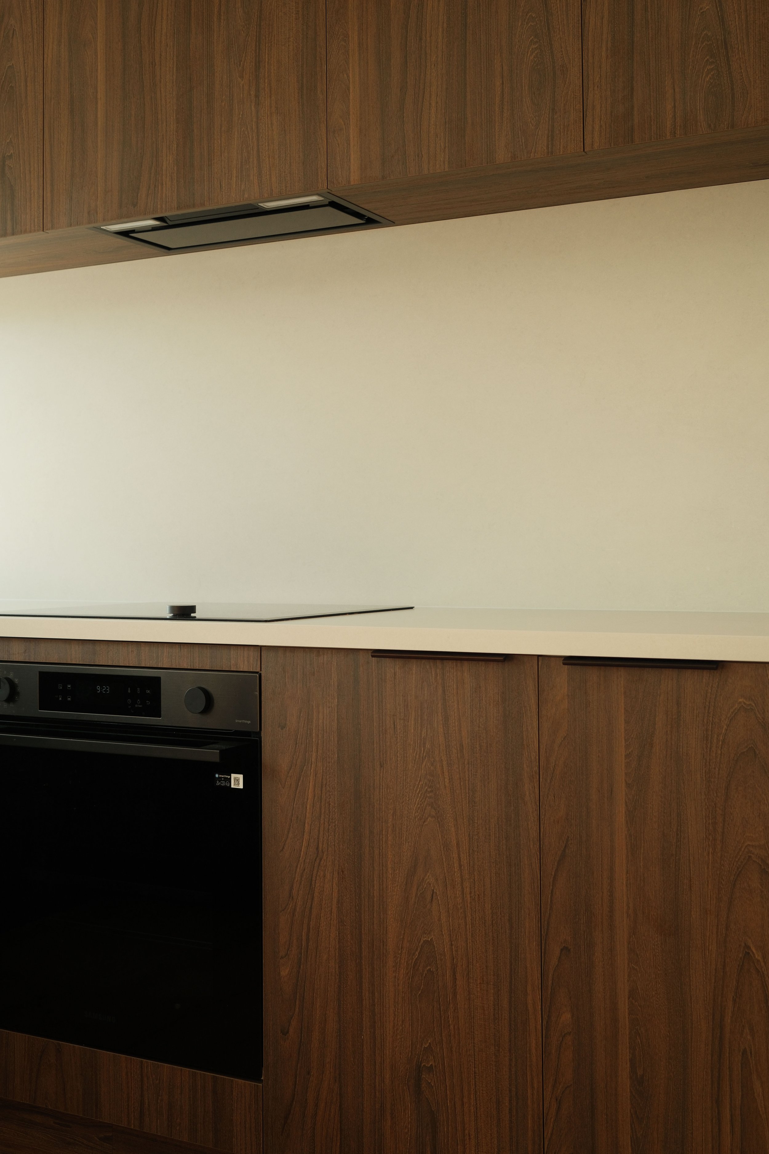 Mount Maunganui kitchen with wooden cabinets, black oven, white countertop, and beige wall.