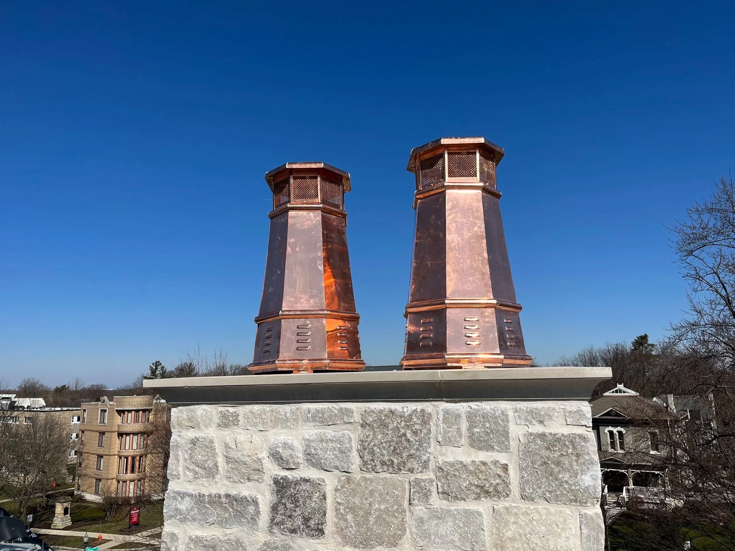 Two custom copper chimneys on a rooftop with a clear blue sky in the background.
