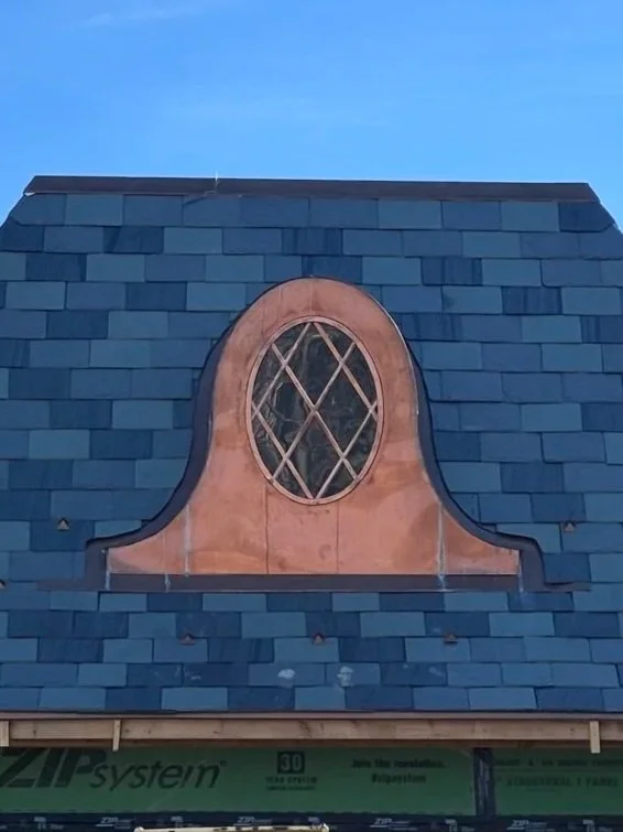 A dormer window with diamond-shaped lattice in a curved, ornate frame on a slate roof.