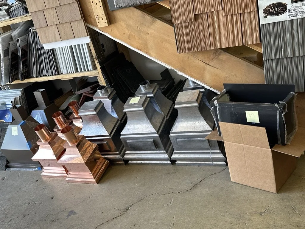 Display of various metal leader heads / scupper boxes, including decorative metal pieces.