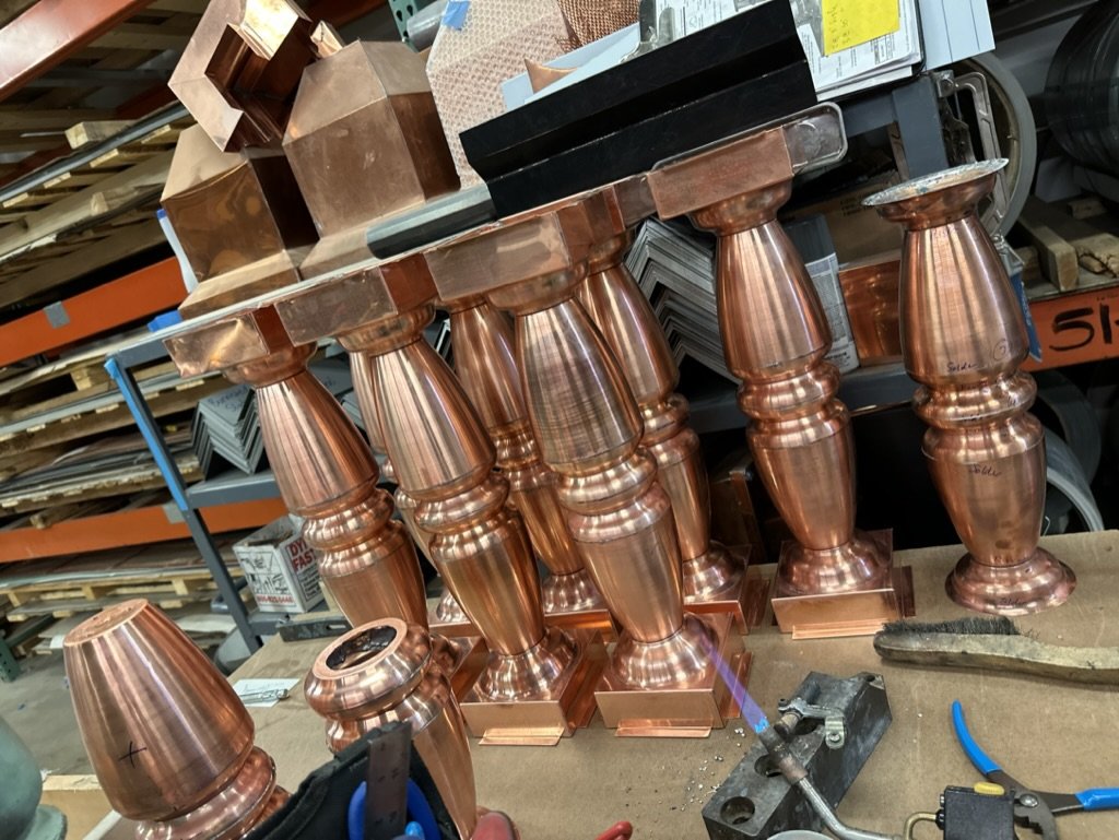 Multiple copper balusters / finials with turned baluster design on a workbench in a workshop.