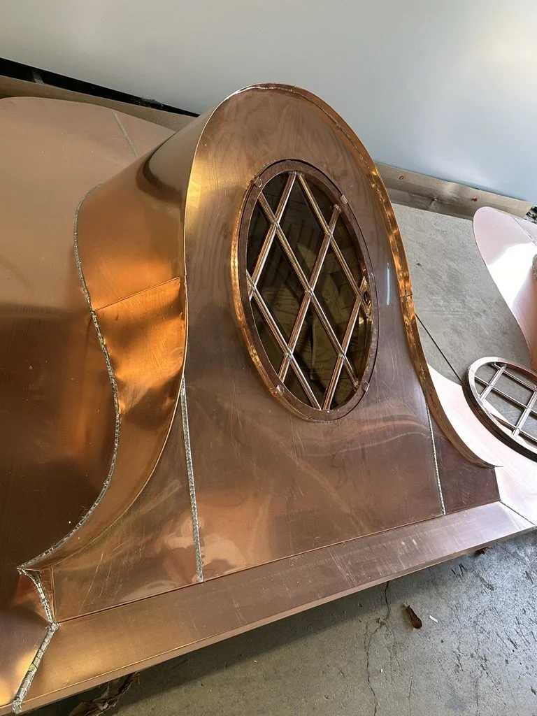 Close-up of a shiny copper metallic dormer with circular openings, metal grid patterns, and smooth curved surfaces, situated on a concrete floor.