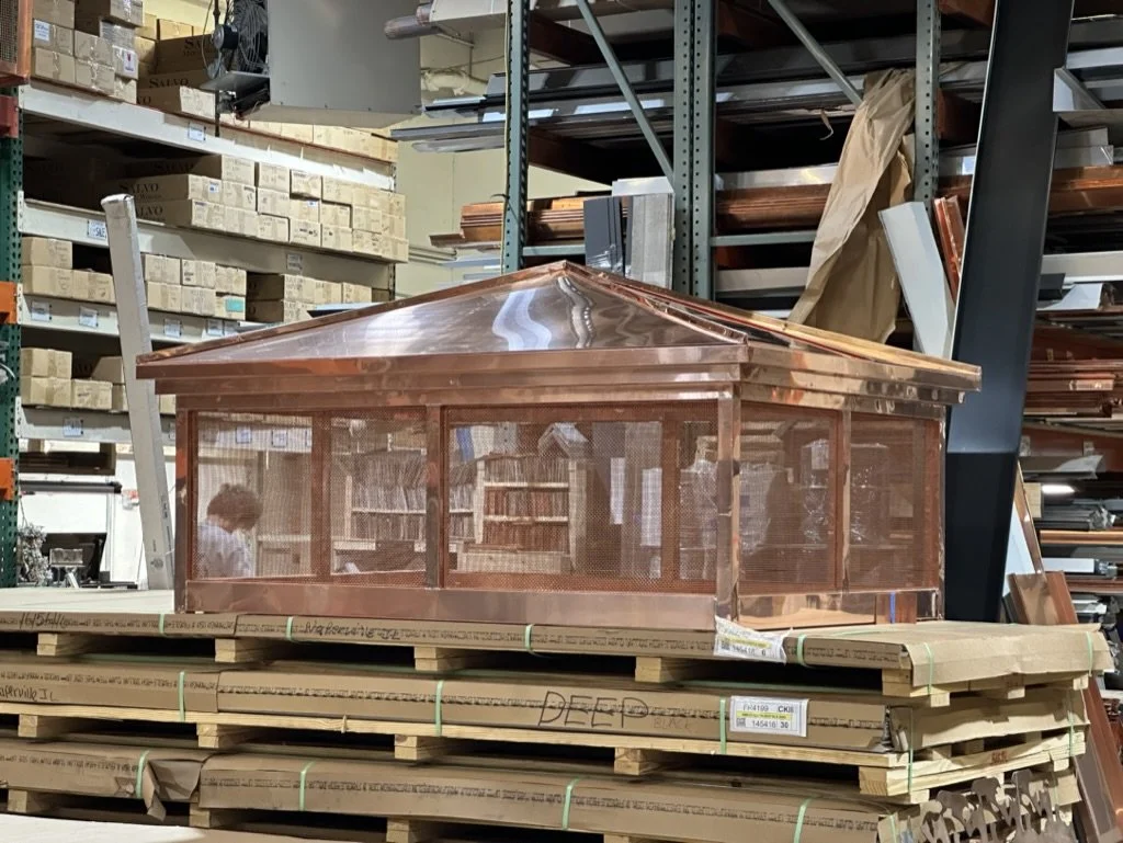 A large copper chimney shroud displayed on wood pallets.