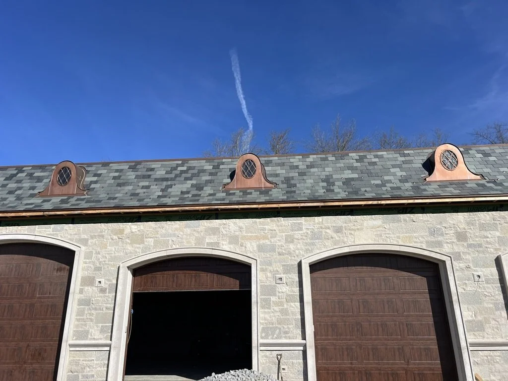 View of a garage with three copper dormer windows on the roof and a blue sky with a contrail above.