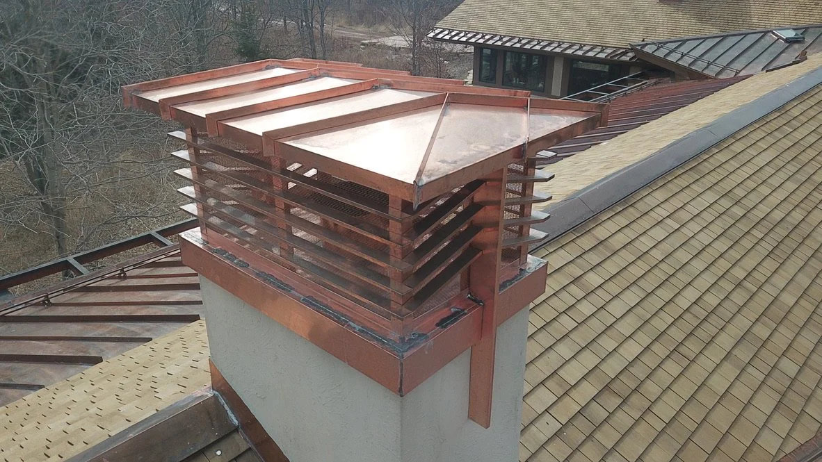 Copper chimney shroud covering a chimney and a section of a sloped tile roof.