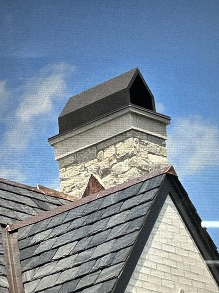 Close-up of a house chimney shroud, roof with gray slate, and a blue sky background.
