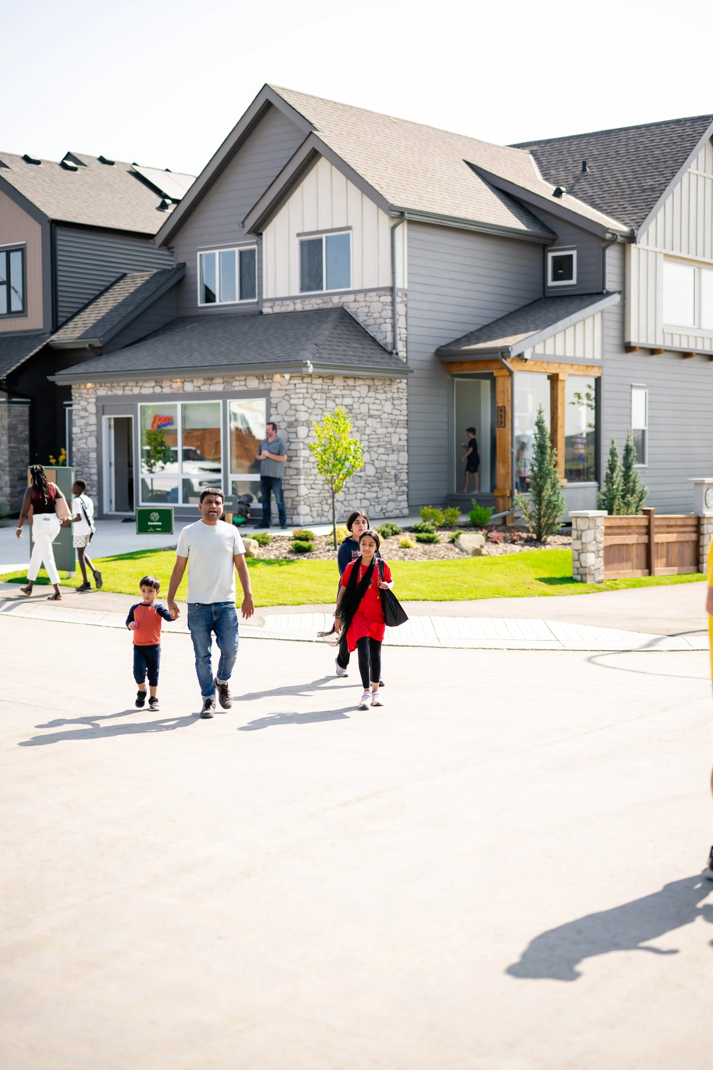 A group of children and adults walking in front of modern houses with a grassy yard on a sunny day.