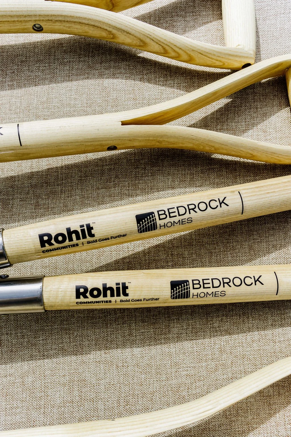 Wooden tool handles with "Rohit Communities" and "Bedrock Homes" branding on a fabric background.
