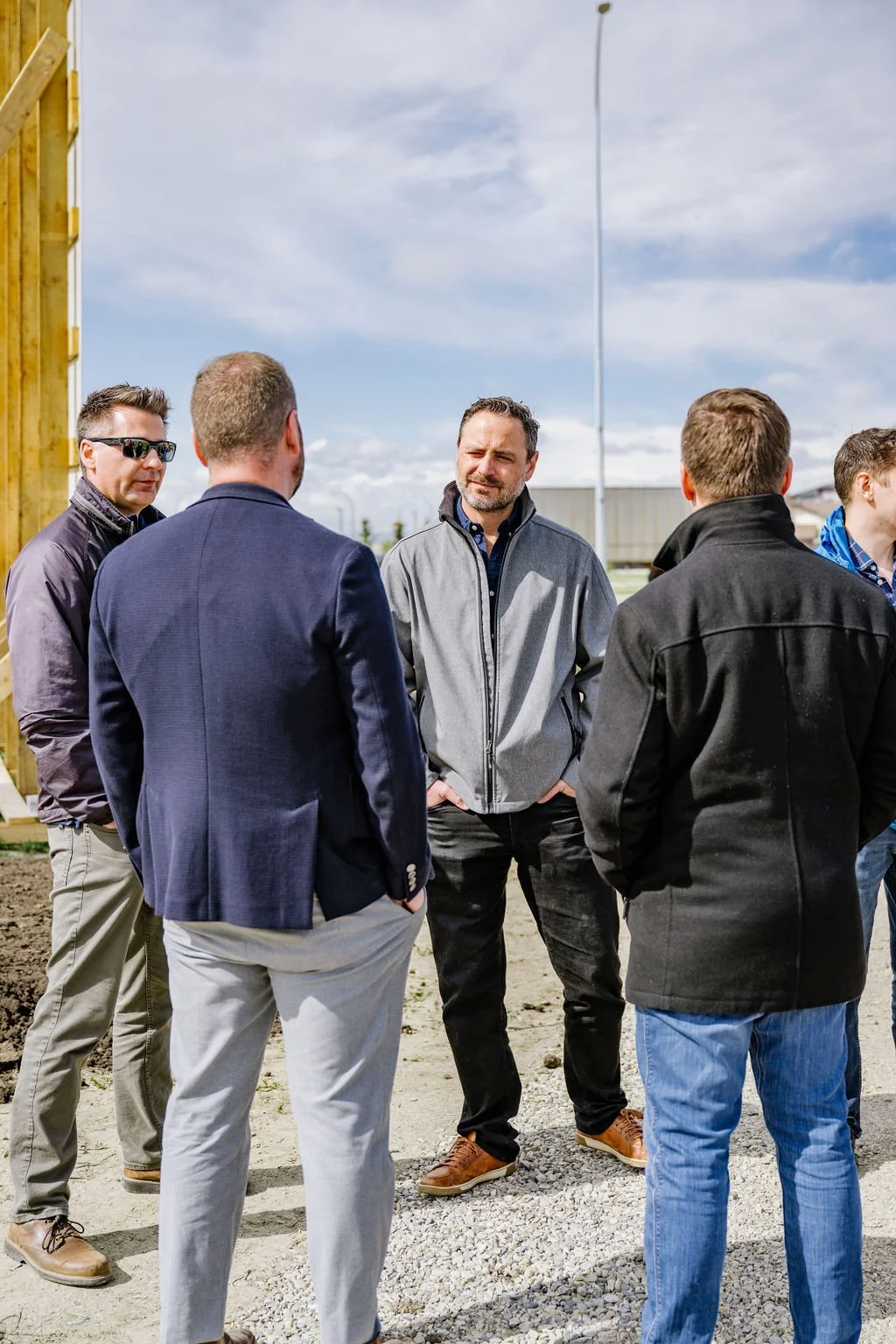 Group of men in outdoor setting, dressed in casual business attire, engaged in conversation.
