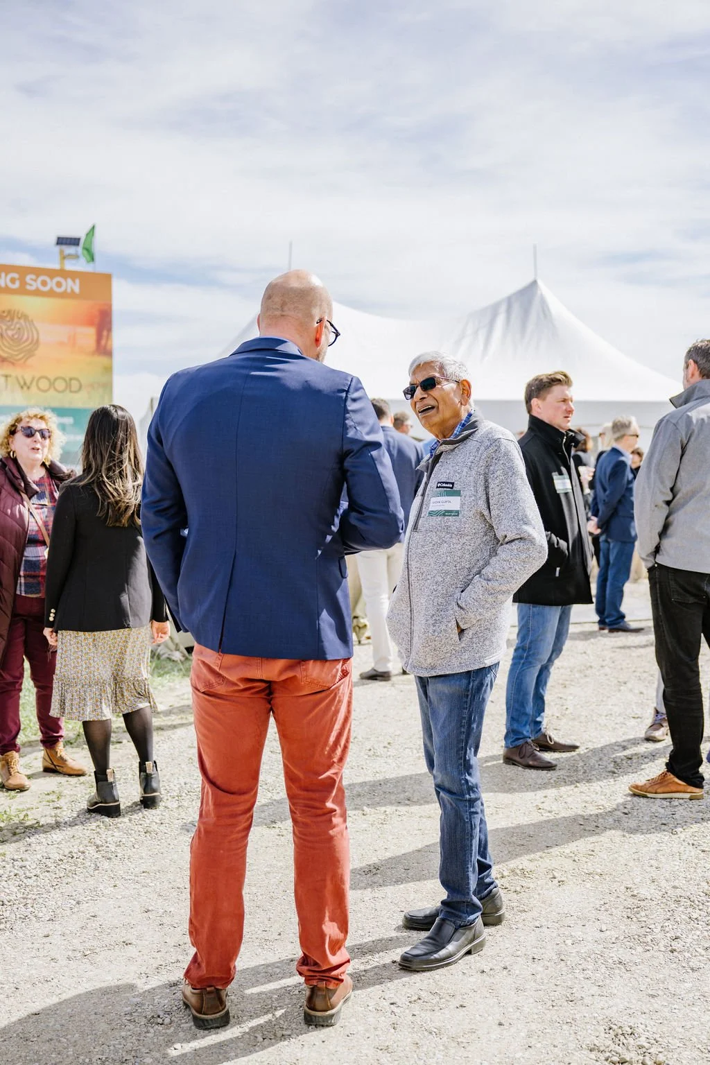 People socializing at an outdoor event, with tents in the background.