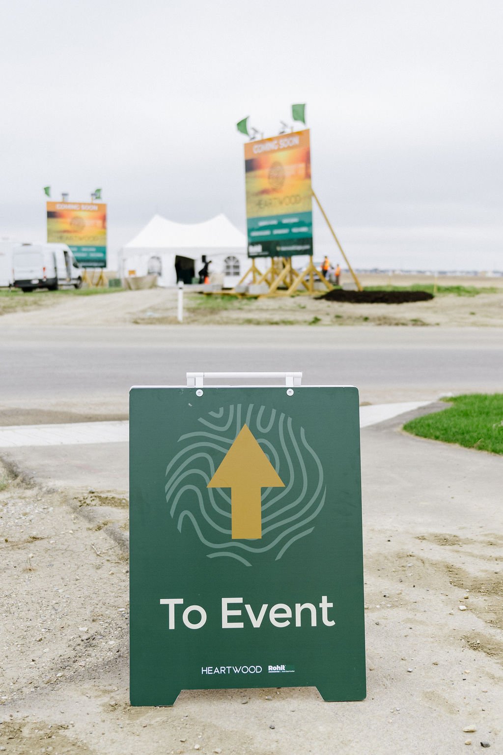 Sign with arrow indicating direction to event near construction site with tents and banners.