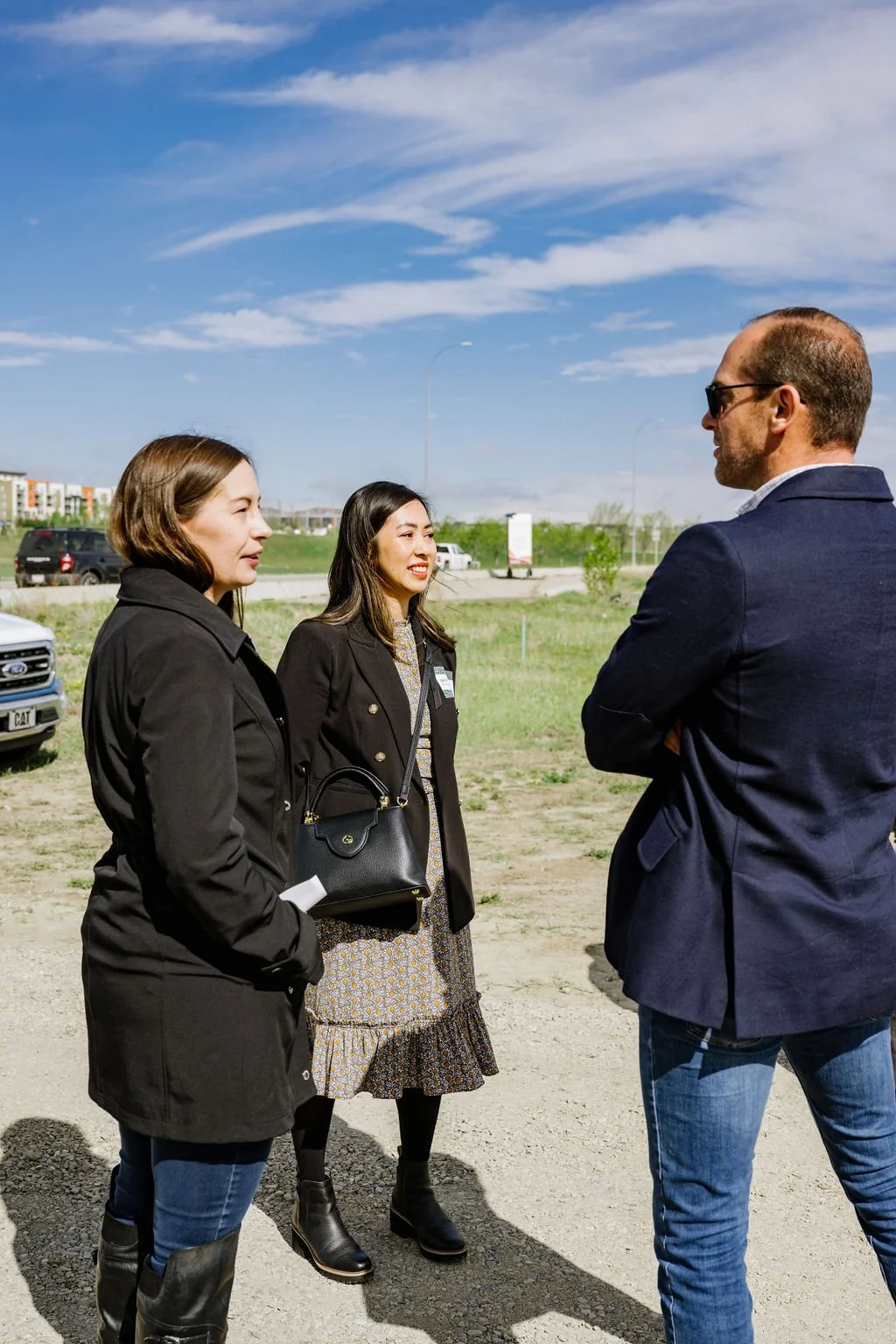 Three people, two women and a man, outside, talking on a sunny day with clear skies and buildings in the background.