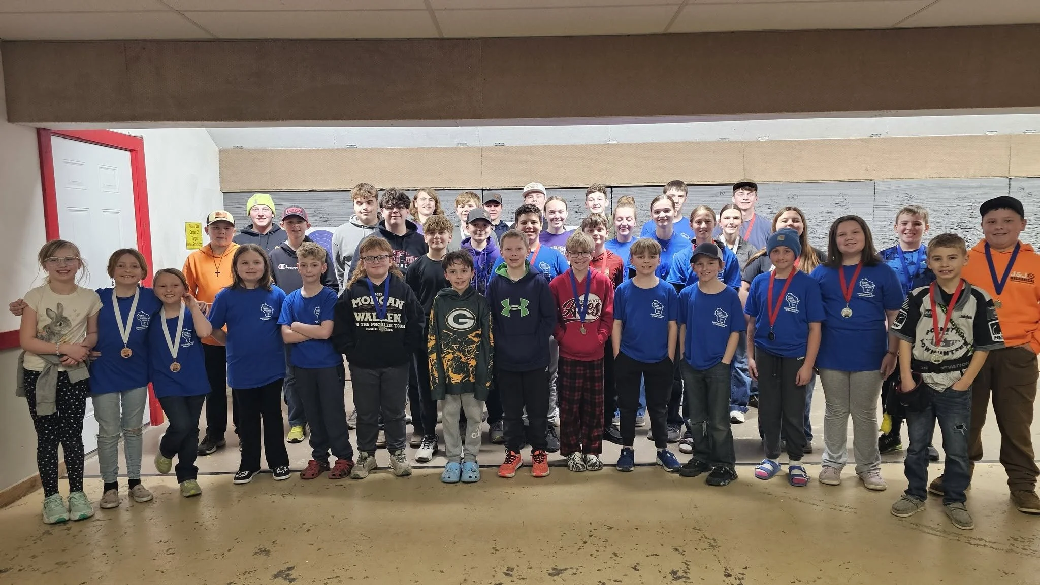Group of children and teenagers posing for a photo indoors, some wearing medals, smiling and standing in front of a backdrop.