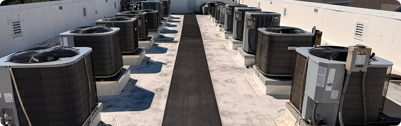 An array of outdoor HVAC air conditioning units installed on a flat rooftop, with a black walkway running through the middle.