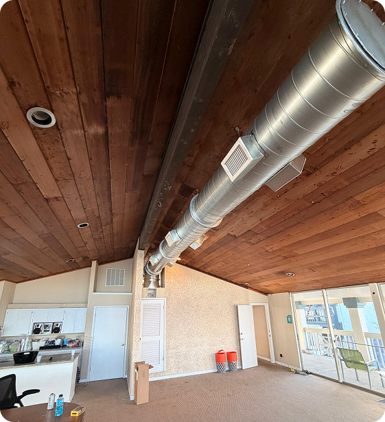Empty apartment room with a wooden ceiling, metal ductwork, and sliding glass doors leading to a balcony with a chair.
