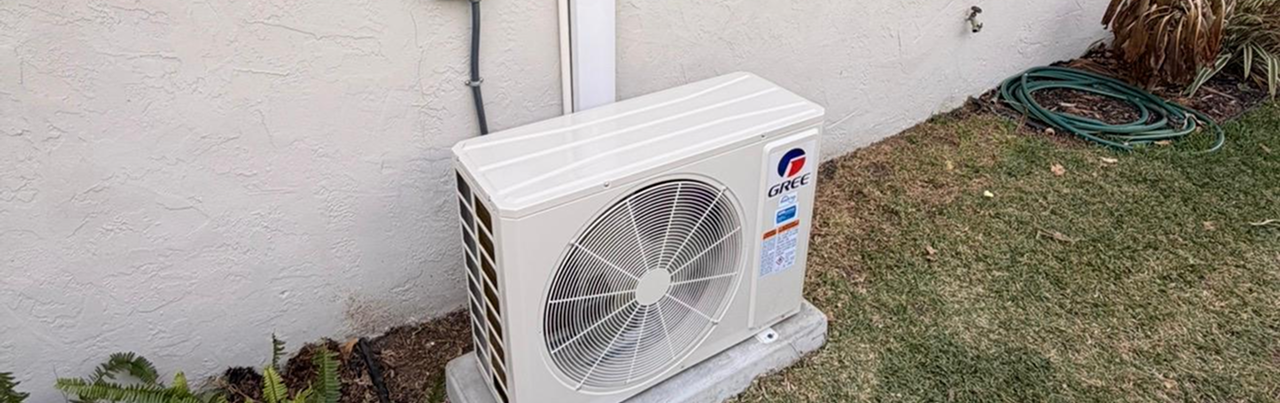 Exterior of an air conditioning unit installed outside a house, positioned on a concrete slab beside a white stucco wall.