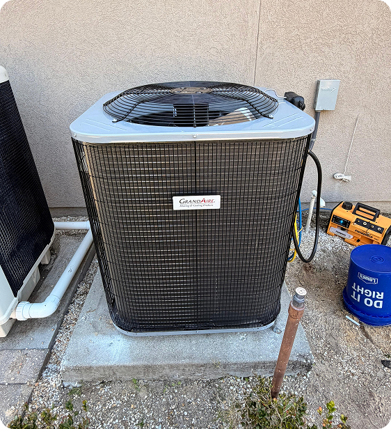 Outdoor air conditioning unit on concrete platform next to a wall, with electrical components and tools nearby.
