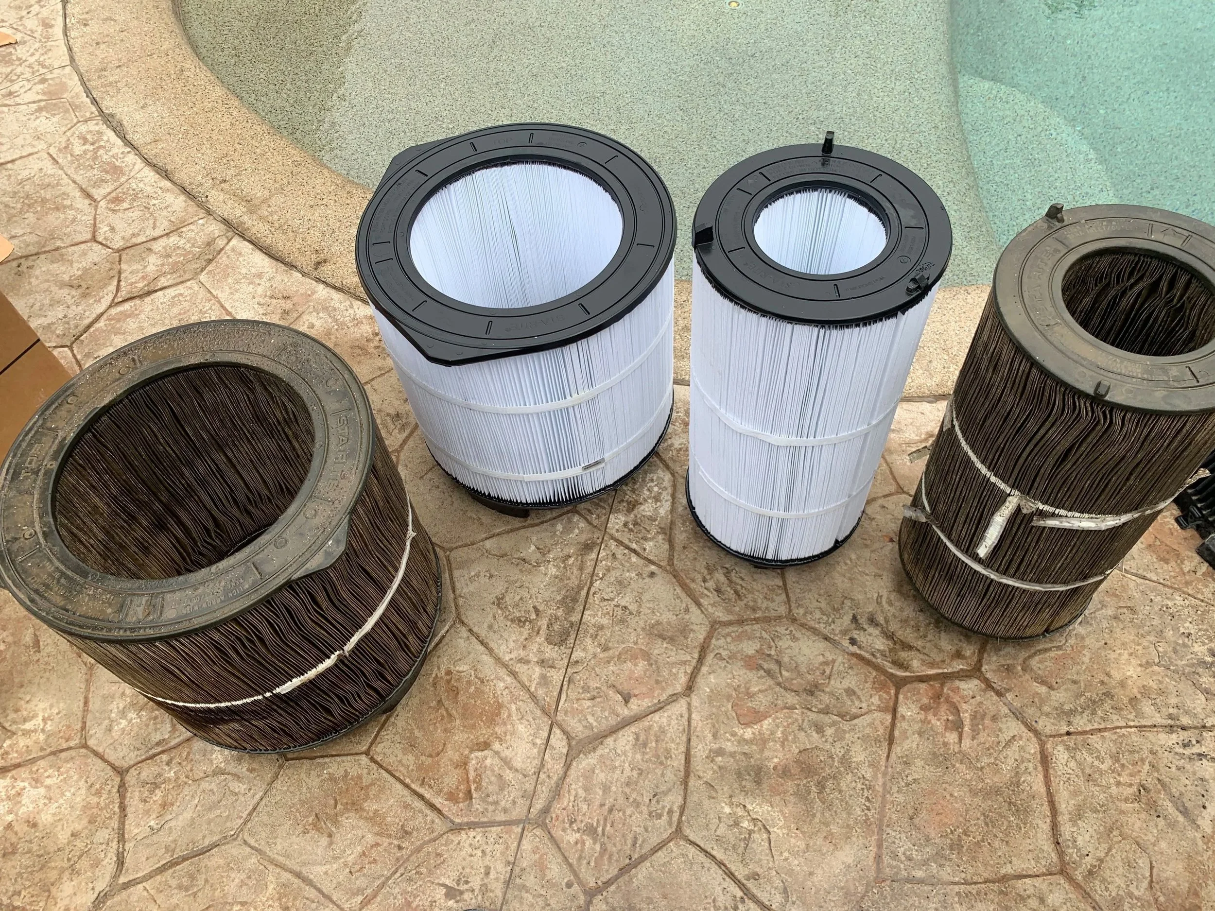 Collection of used pool filters placed on a stone-tiled floor near a swimming pool.