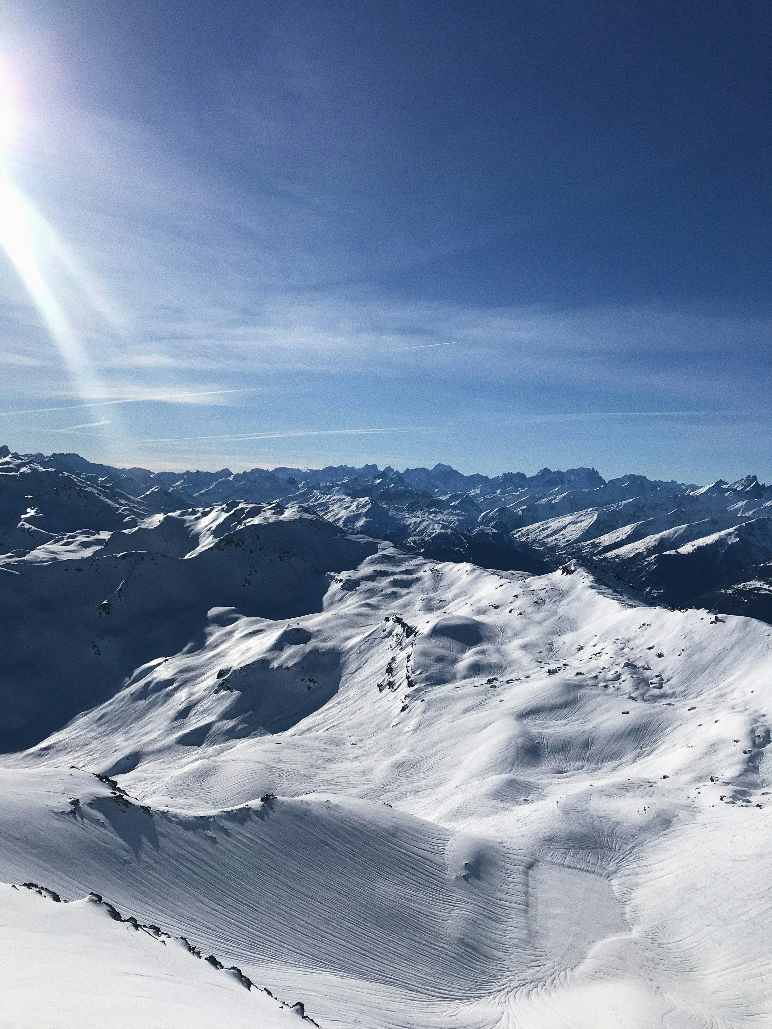 Snow-covered mountain peaks and ridges under a bright blue sky with a few wispy clouds.